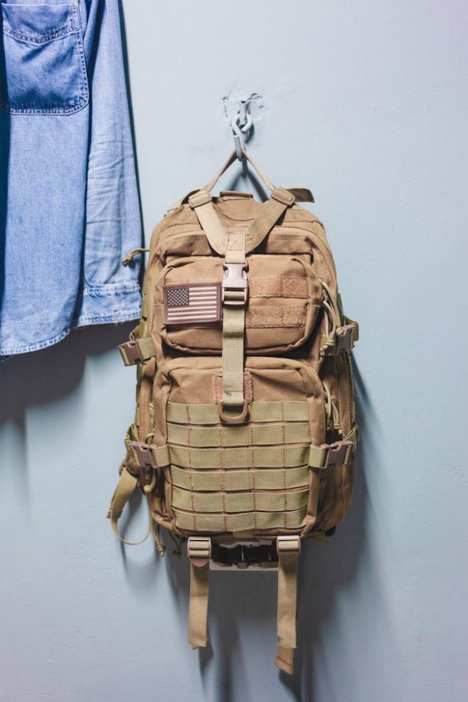 A rugged military style backpack hangs on a hook next to a denim jacket indoors.